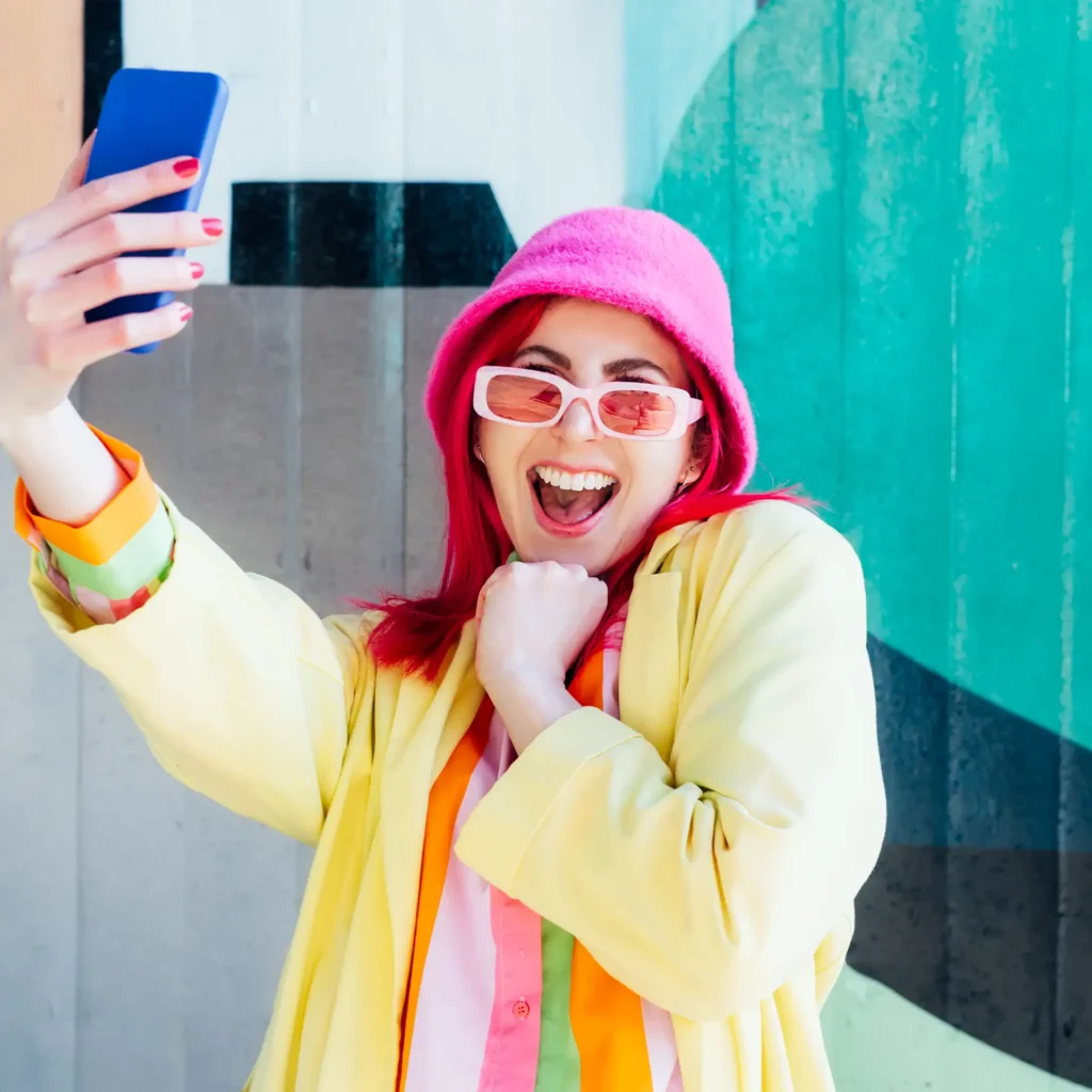 Creatorin mit pinkem Hut filmt sich lachend mit dem Handy